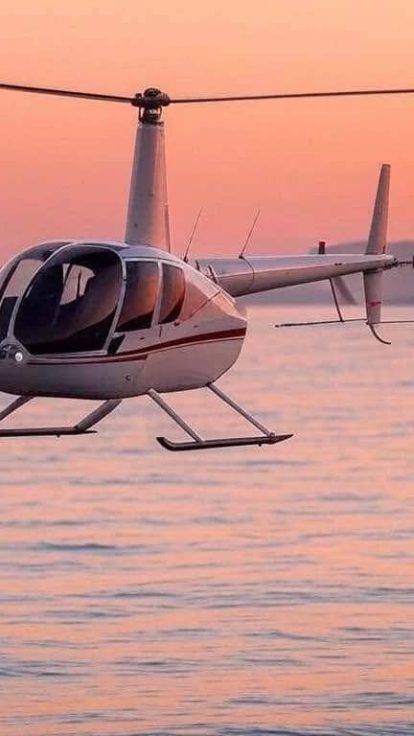 R44 en vol au ras de la mer au coucher du soleil